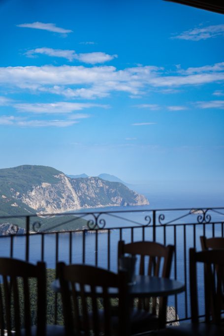 Ausblick von einer Terrasse auf felsige Küste und weites Wasser unter blauem Himmel.