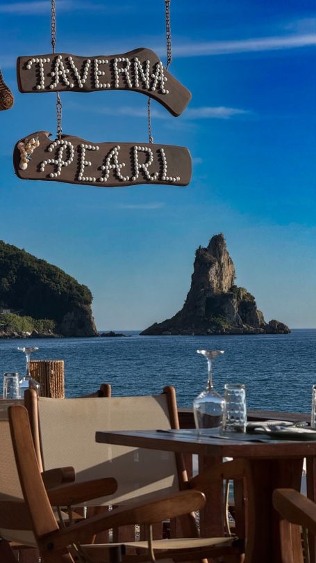 Holztäfelchen der Taverne "Pearl" mit Meerblick und Felsen im Hintergrund.